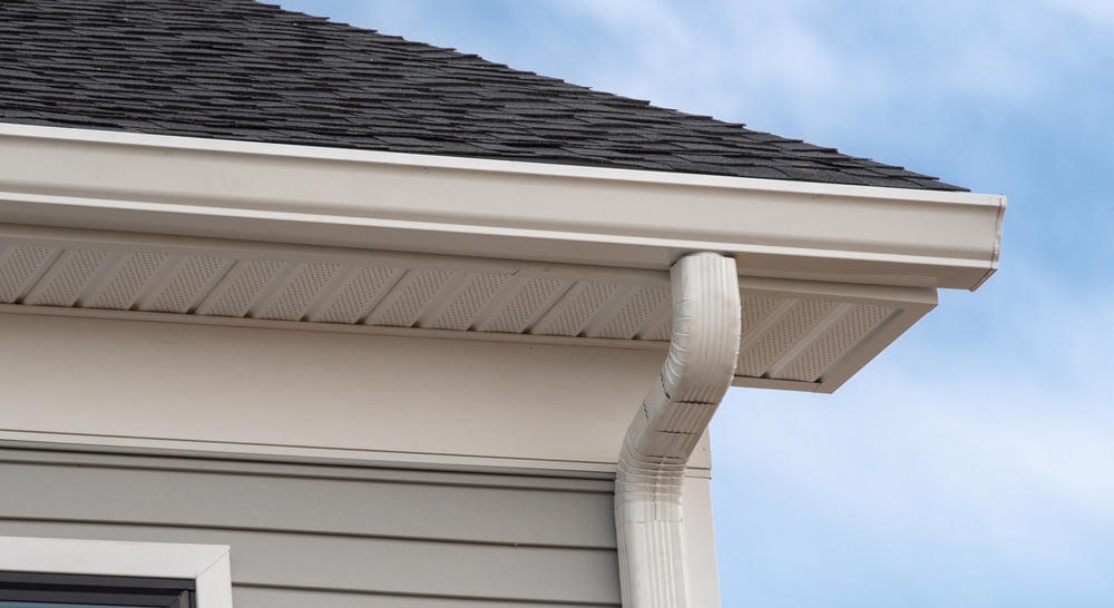 Close-up of roof edge with gutter and downspout system guiding rainwater away from home exterior