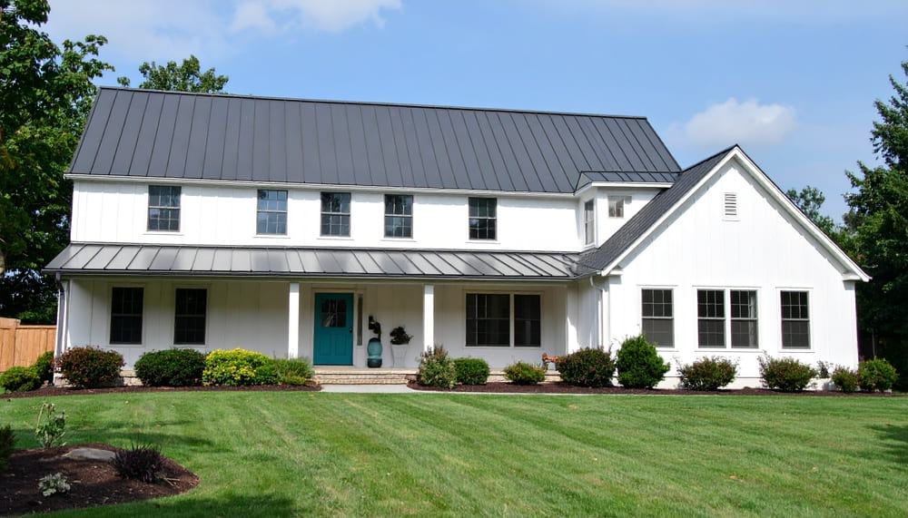White house with metal roof and landscaped yard illustrating energy-efficient roofing that reflects heat and lowers cooling costs